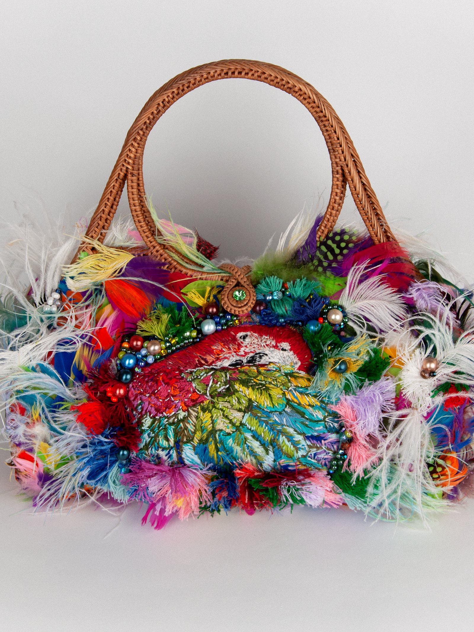 Le Jardin de Plumes de Maison Delmon Paris, avec un ara brodé multicolore, de longues plumes blanches et des anses tressées.