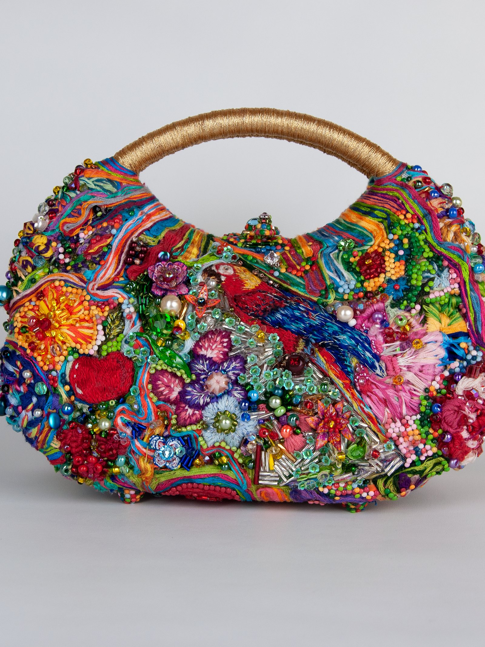 Le Jardin de Soie de Maison Delmon Paris, sac arrondi à anses dorées, brodé d’un ara, de fleurs et de fruits multicolores.